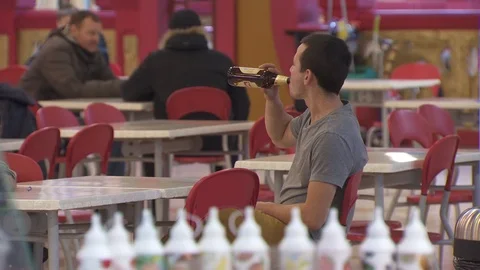 A man sits at a table in fast food and drinks beer from a bottle Stock Footage 113798515