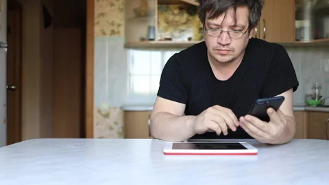 A man sits at a table. in front of him tablet and in the hands of the phone Stock Footage 130941526