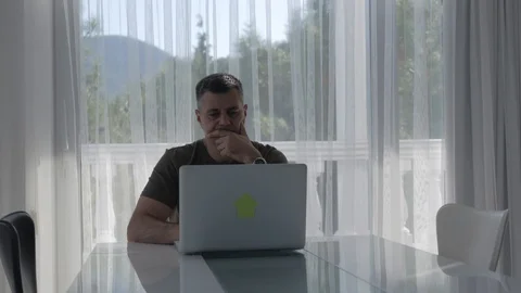 A man sits at a table in front of a large window with a beautiful forest Video stock 116734466