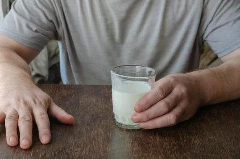 Man sits at table with half-empty glass of kefir. Stock Photos