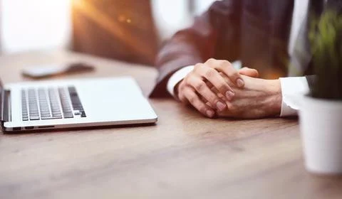 A man sits at a table with his hands clasped together close-up Stock Photos