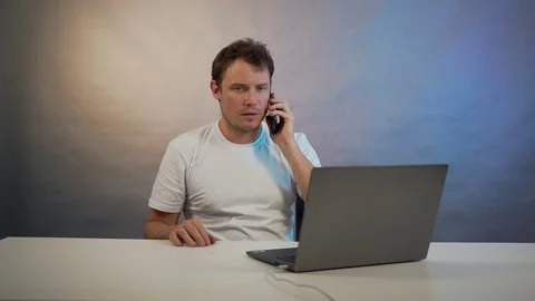A man sits at a table with laptop and talking on the phone Stock Footage 128998288