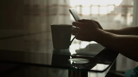 A man sits at a table with a mobile phone in his hands next to a mug Stock Footage 129854318