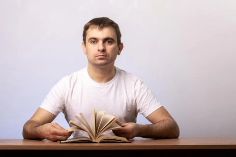 Man sits at a table with an open book against the background of a white wall. Stock Photos