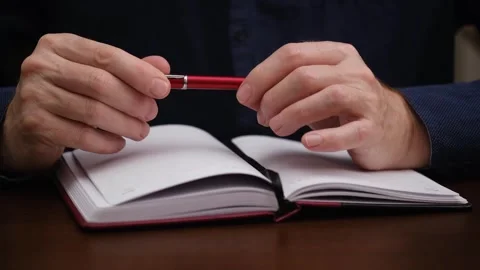 Man sits table over an notebook and twirls pen in his hands closeup. front view. Video stock 300229055