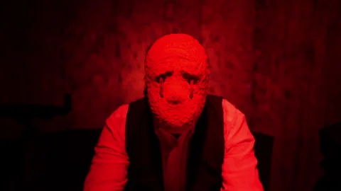 A man sits at a table, removes the mask of an evil creature. Under the mask is Stock Footage 242431983