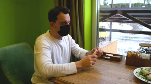A man sits at a table in a restaurant wearing a mask, takes an antiseptic and Stock Footage 169961812