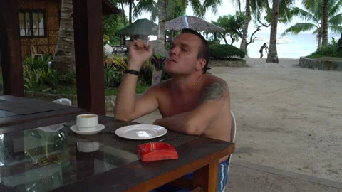 A man sits at a table on the street with a cup of coffee and smokes Stock Footage 91368321