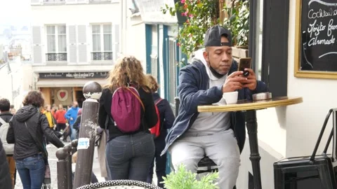 Man sits at the Table of Street Restaurant with Mobile Phone on Montmartre Paris Stock Footage 164595620