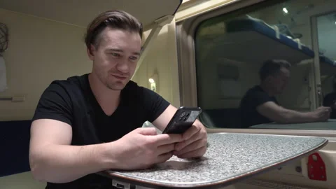 Man sits at a table in a train carriage and uses a smartphone. Stock Footage 263531743