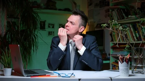 A man sits at a table in the workplace, biting his nails. Vídeos de archivo 128027910