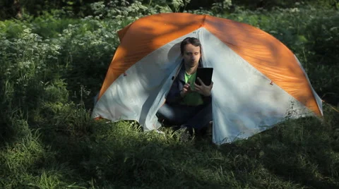 A man sits in a tent and making a video call on the tablet. Morning in the Stock Footage 64313933