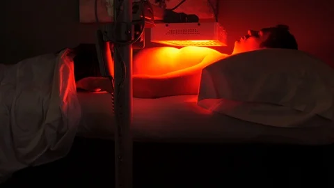 Man sits under the red light therapy with lamp on chest Stockbeeldmateriaal 107758111