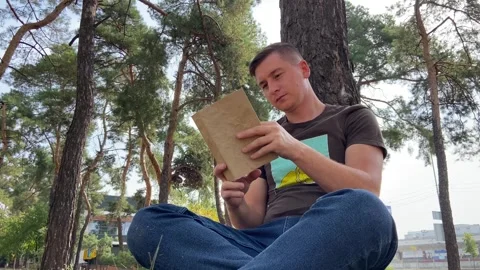 A man sits under a tree and reads a book. The boy gains knowledge in the forest Stock Footage 283639541