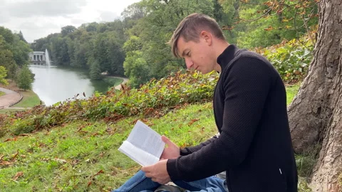 A man sits under a tree and reads a book. The boy gains knowledge in the forest Stock Footage 287329545