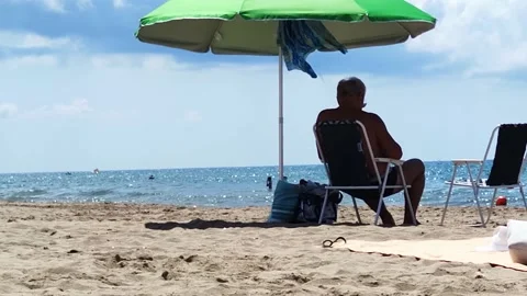 A man sits under an umbrella on the beach Stock Footage 219570735