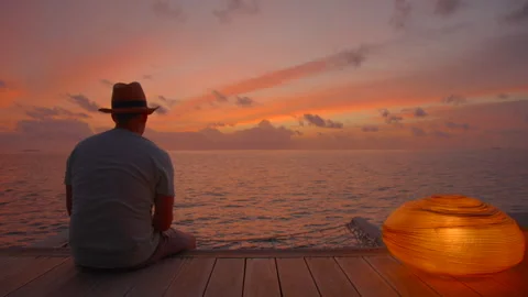 Man sits on villa decking enjoying sunset Stock Footage 247282226
