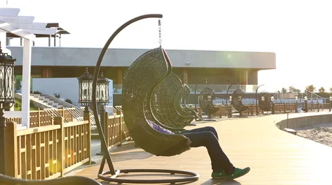 Man sits on wickered swing slightly rolling next to bungalow wall. Stock Footage 63614857