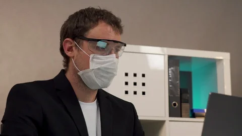 A man sits working at a laptop in a protective mask and goggles Vídeo Stock 129049288