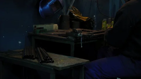 The man sits in the workshop and puts the steel elements on the workbench Stock Footage 128590202