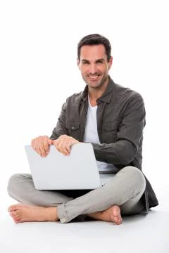 Man sitted on the floor, smiling at camera, holding his laptop with both hand Stock Photos
