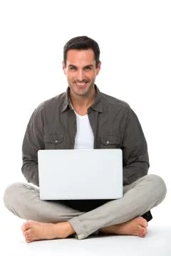 Man sitted on the floor, smiling at camera and working with his laptop Stock Photos