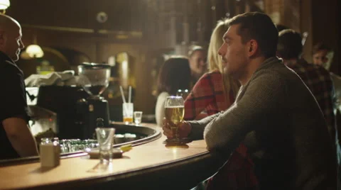 Man sitting alone with beer in a bar while people are having good time Stock Footage