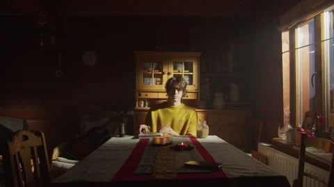 Man sitting alone at dining room table in cozy evening light Stock Footage 319946699