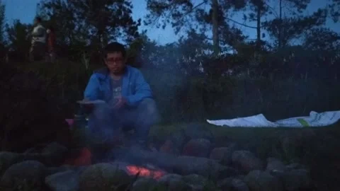 A man sitting alone in front of campfire bonfire at indonesian family fun campin Stock Footage 151301837