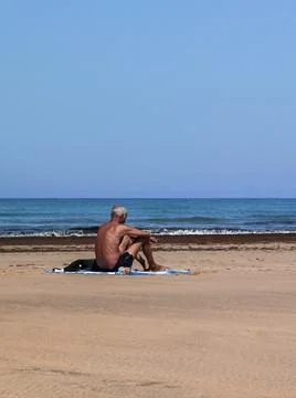 Man sitting alone right next to the ocean shore Stock Photos