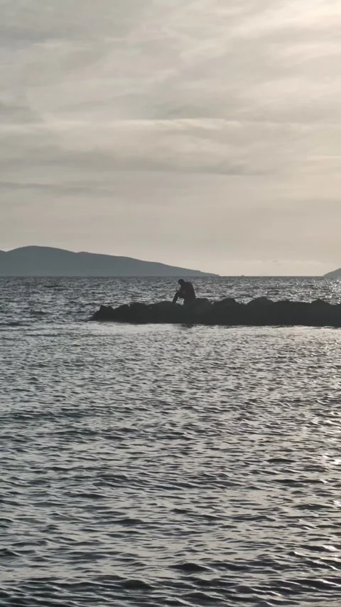 A man sitting alone on the rocks by the sea taking photos. Stock Footage 289543294