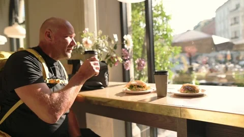 Man sitting alone at sunny cafe table with sandwich and coffee Stock Footage 320089874