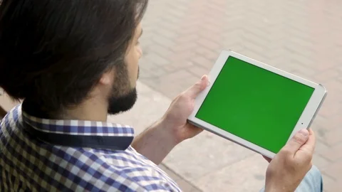 Man is sitting and holding pad in hands. Then he starts to slide on screen three Stock Footage 99740040