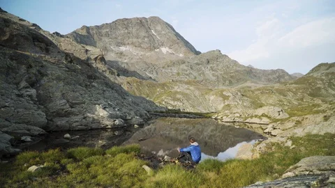 Man sitting and resting at small lake and throwing rock into water, 4K Stock Footage 129613922