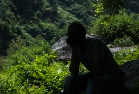 A Man Sitting and Thinking in a Forest, a Rock in the Background, Silhouette Stock Photos