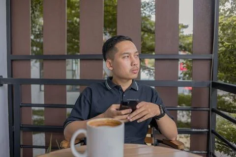 Man Sitting And Thinking While Holding Phone With Coffee On The Table, Glan.. Stock Photos