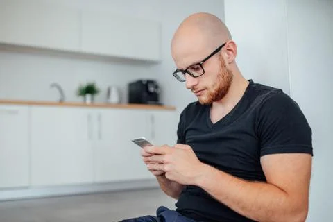Man is sitting and using mobile phone. Kitchen background. Stock Photos