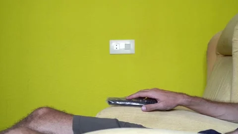 Man sitting in an armchair using the remote to change the TV channel. Stock Footage 159969396