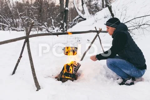 Man sitting aroung camping fire, looking into fire, boiling a water in pot. G Stock Photos