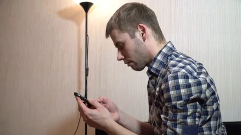 Man is sitting on the background of a home lamp in his house and is looking at a Video stock 86159380