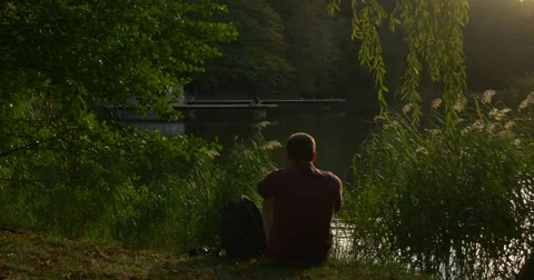 Man is Sitting Backpack is Close to Man Observing The Rippling Water Man Has Stock Footage 55417773