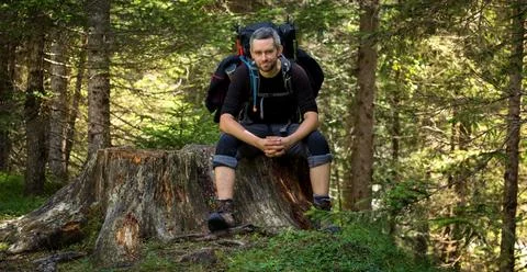 A man sitting with a backpack on a tree trunk by the trail Stock Photos