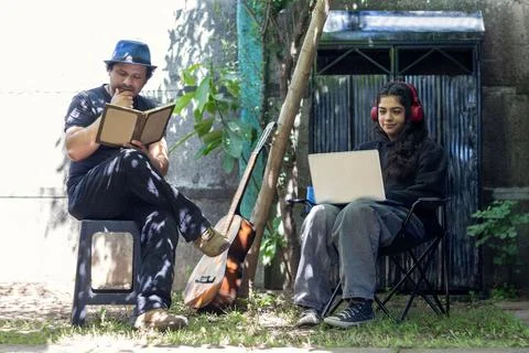 Man sitting in the backyard reads a book next to his daughter Stock Photos