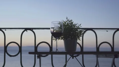 A man is sitting on the balcony and drinking red wine on the background of the 스톡 동영상 85213620