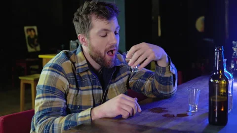 A man sitting at a bar drinking shots or vodka. Drinking, going out, inclusivity Stock Footage 231681750