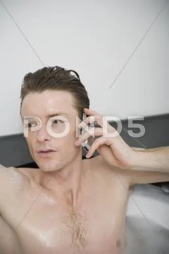 Man sitting in a bathtub and holding a mobile phone Stock Photos