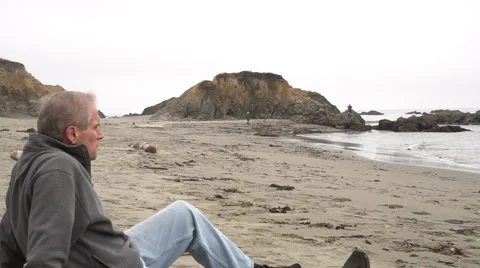 Man sitting on beach alone and wiping eyes Видео 67877379