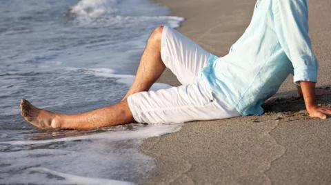 Man sitting on beach in the sunrise light. Stock Photos