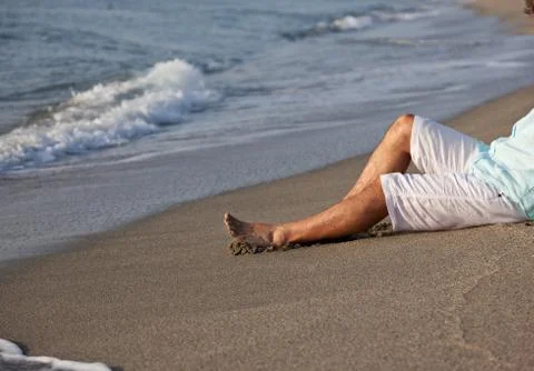 Man sitting on beach in the sunrise light. Stock Photos