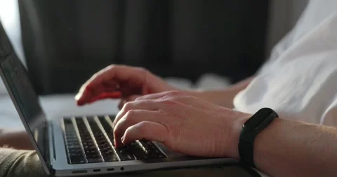 The man is sitting on the bed and working on a laptop that lies on his lap Stock Footage 302901295
